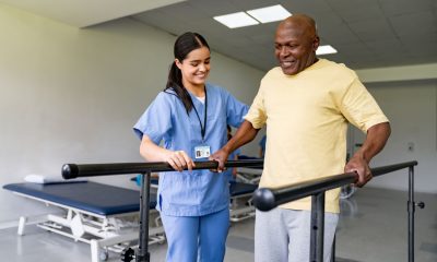 Happy physical therapist helping an African American senior man walking on bars at a rehabilitation center