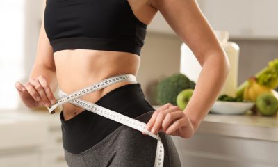 Weight loss. Woman measuring waist with tape in kitchen, closeup